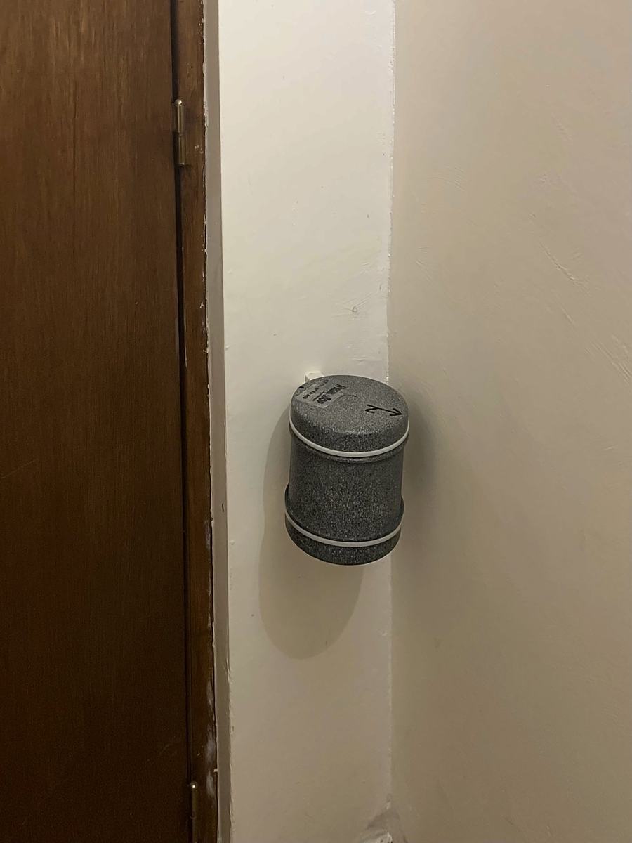 Boîtier gris fixé au mur d'un couloir, près d'une porte en bois.