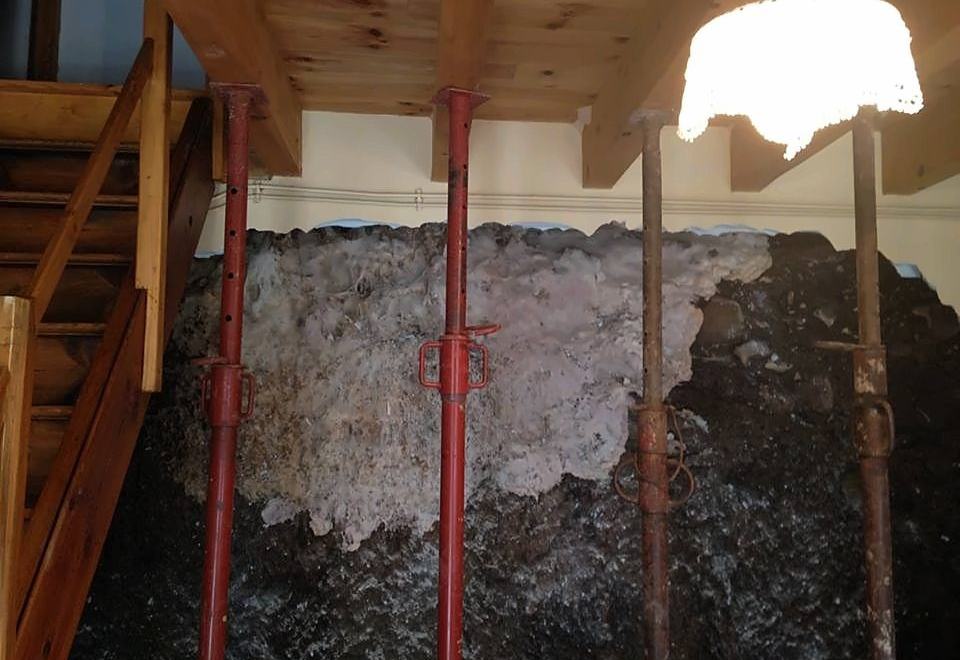 Chantier de traitement de la mérule : plancher soutenu par des étais rouges devant un mur recouvert de champignon